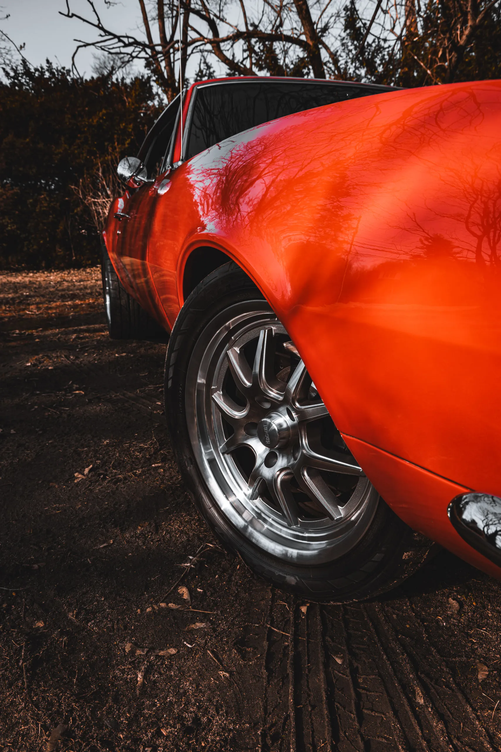 Low rear-quarter detail of a red Camaro's polished wheel and flared arch