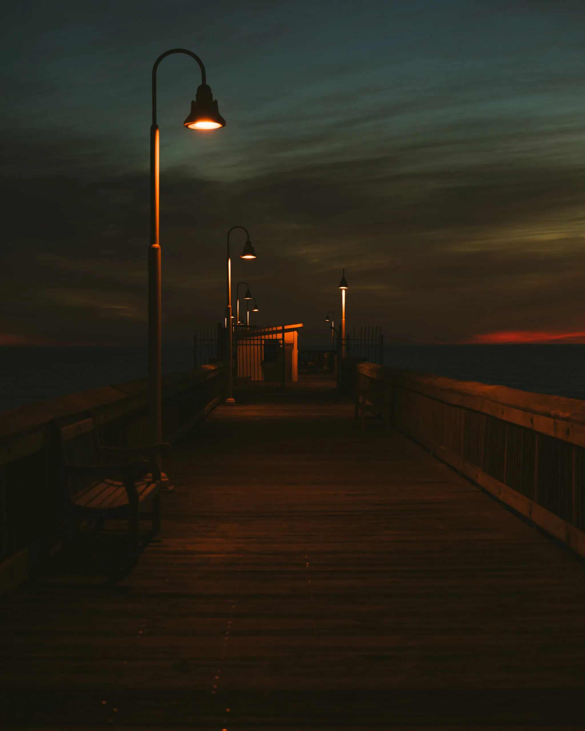 A wooden pier stretches into dusk under a row of lamps