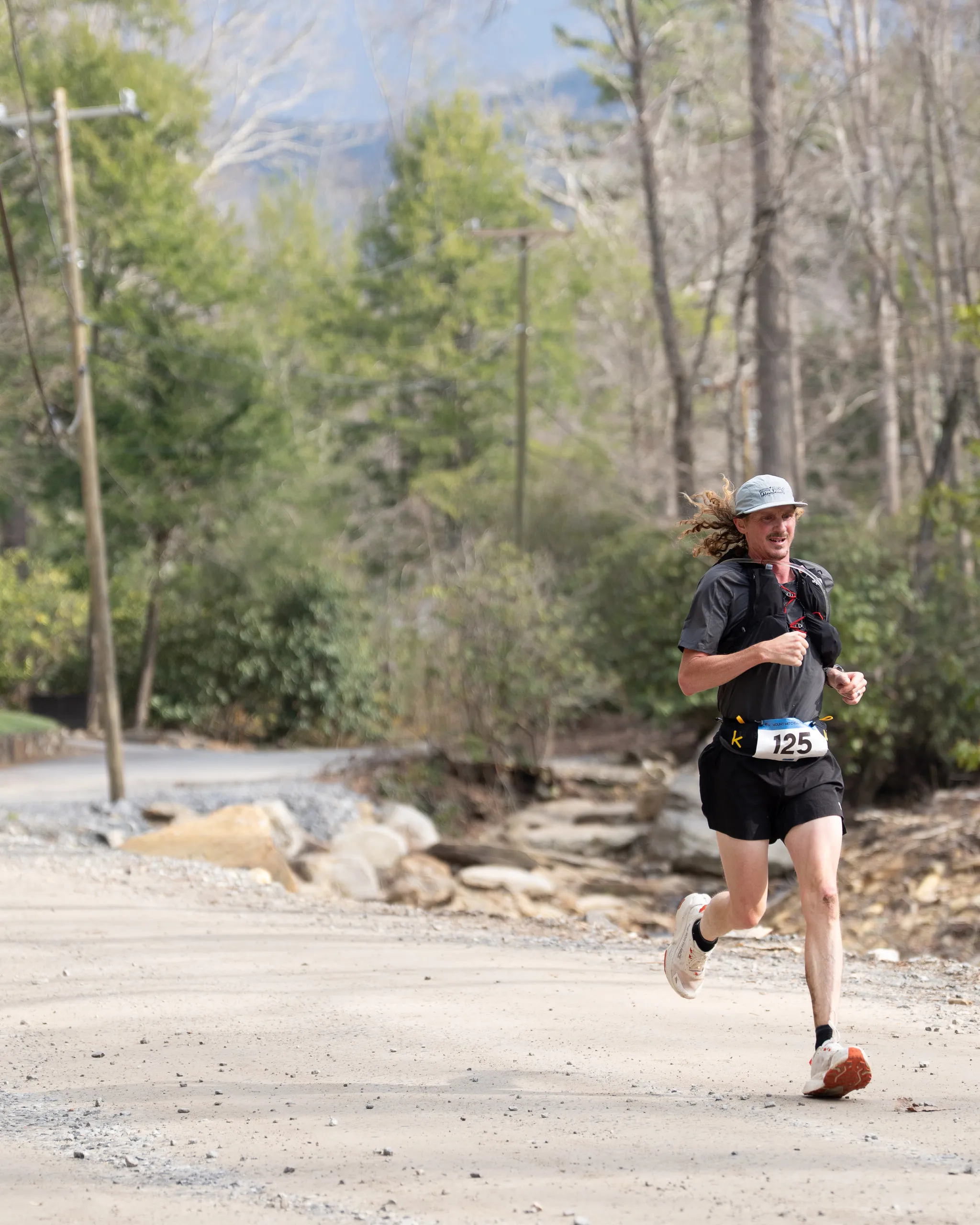 A runner in a race bib pushes up a gravel road between bare trees
