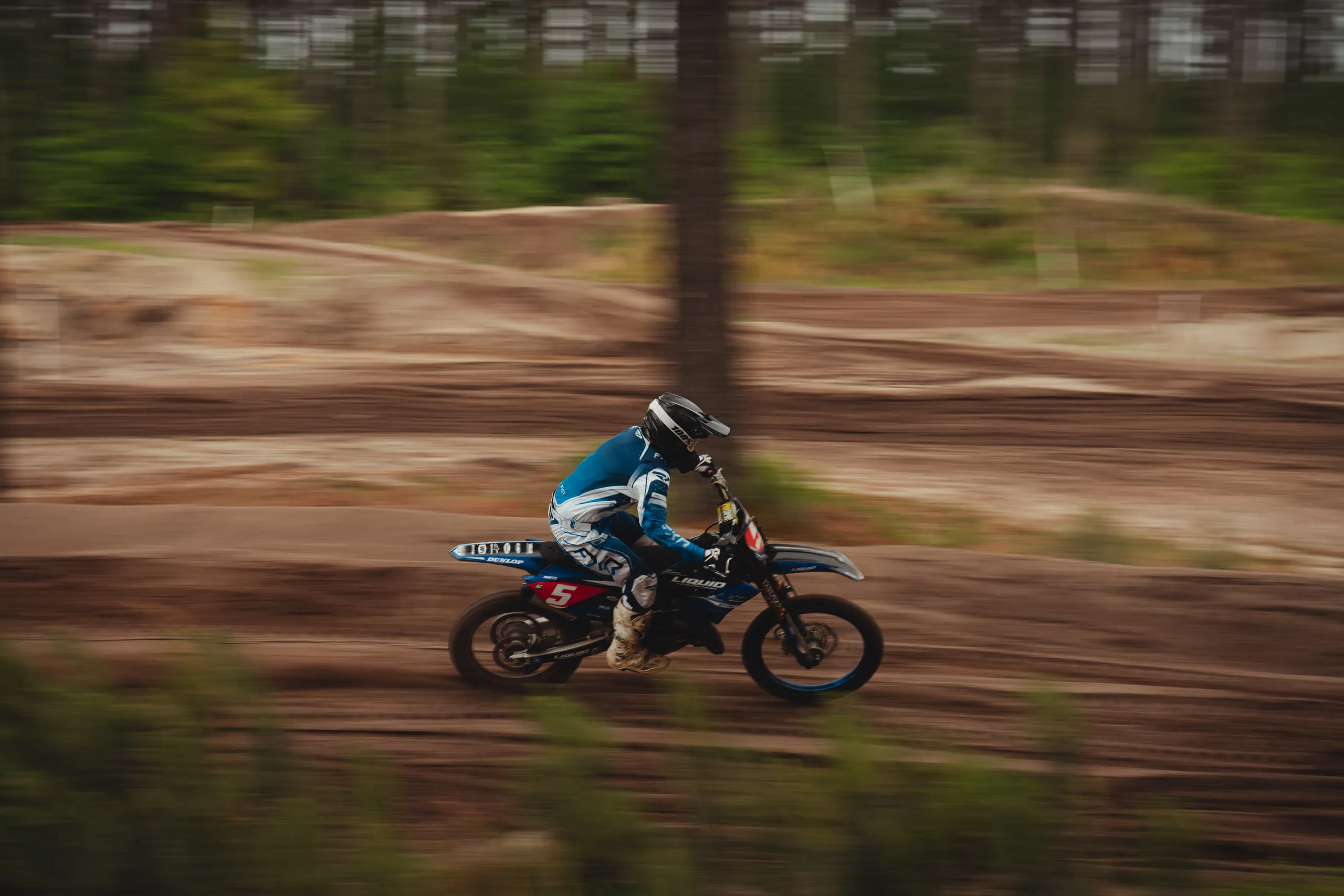 A rider blurs past on a straight, the trackside trees smeared by the panning shot