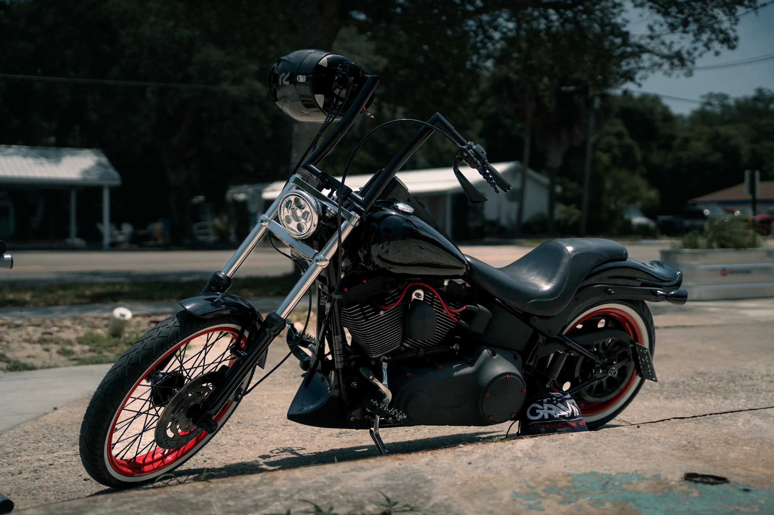 A blacked-out custom motorcycle with red wheel accents parked on cracked asphalt