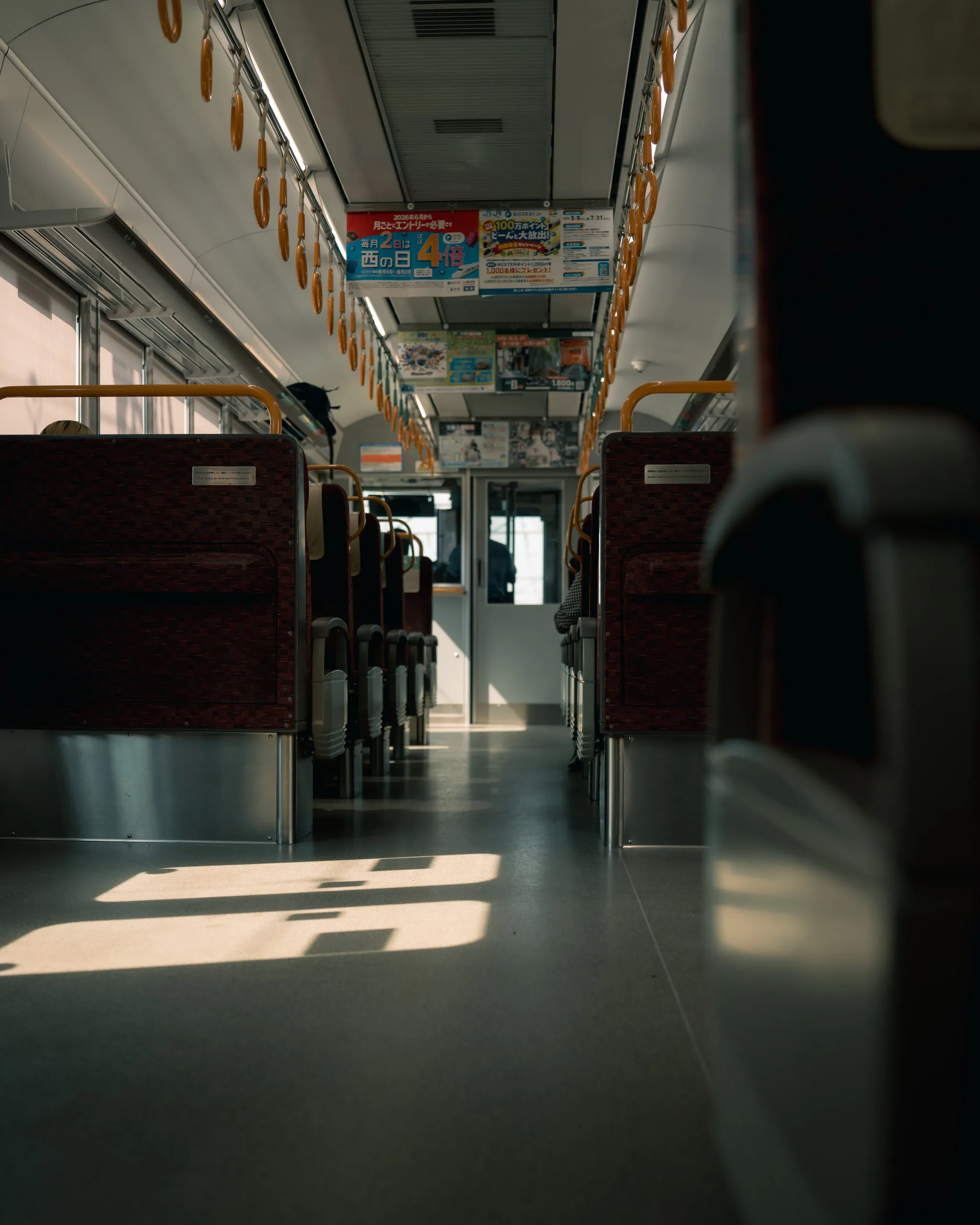 Sunlight falls in bright patches down the aisle of an empty commuter train