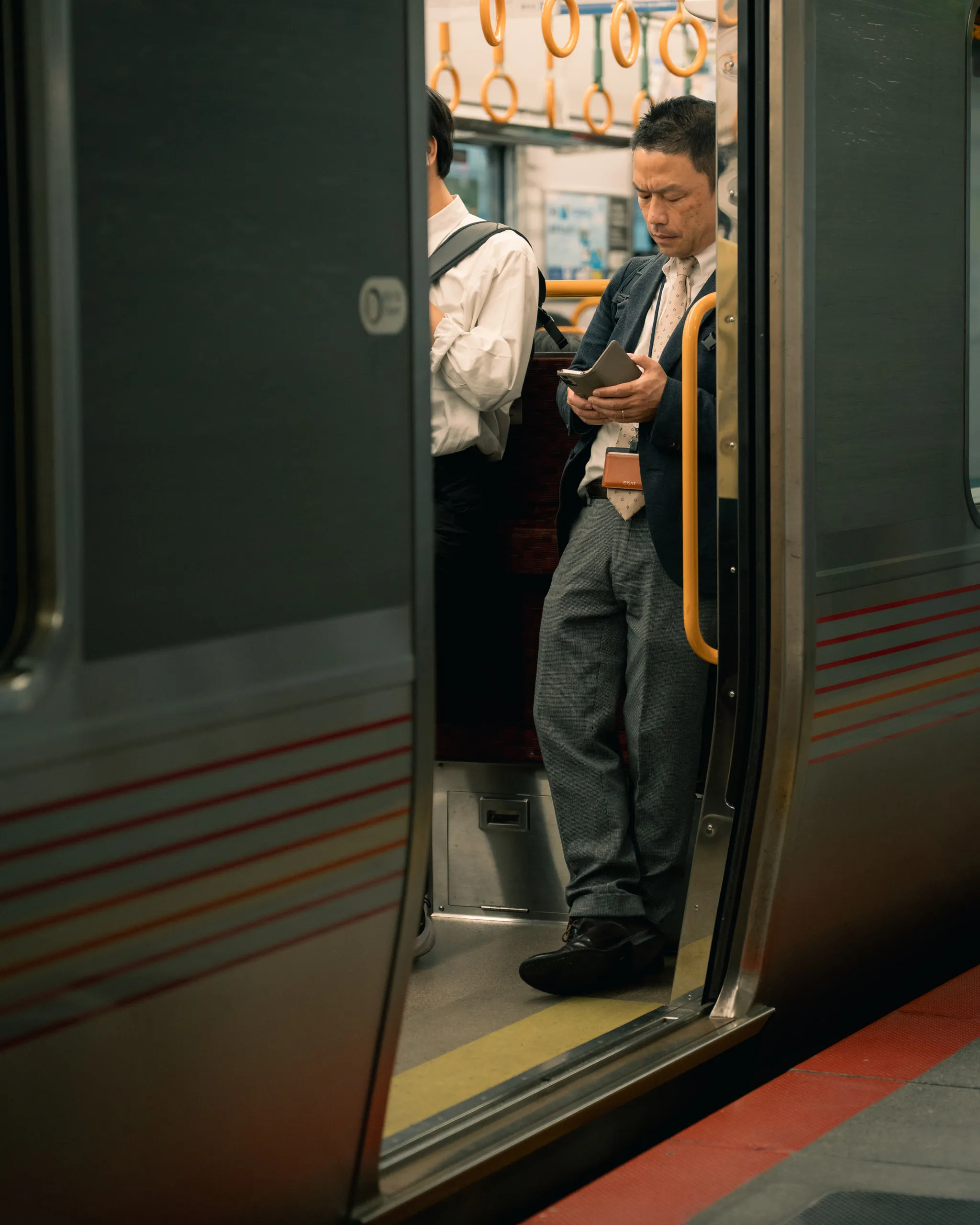 A commuter stands in a train doorway checking his phone as the doors hold open