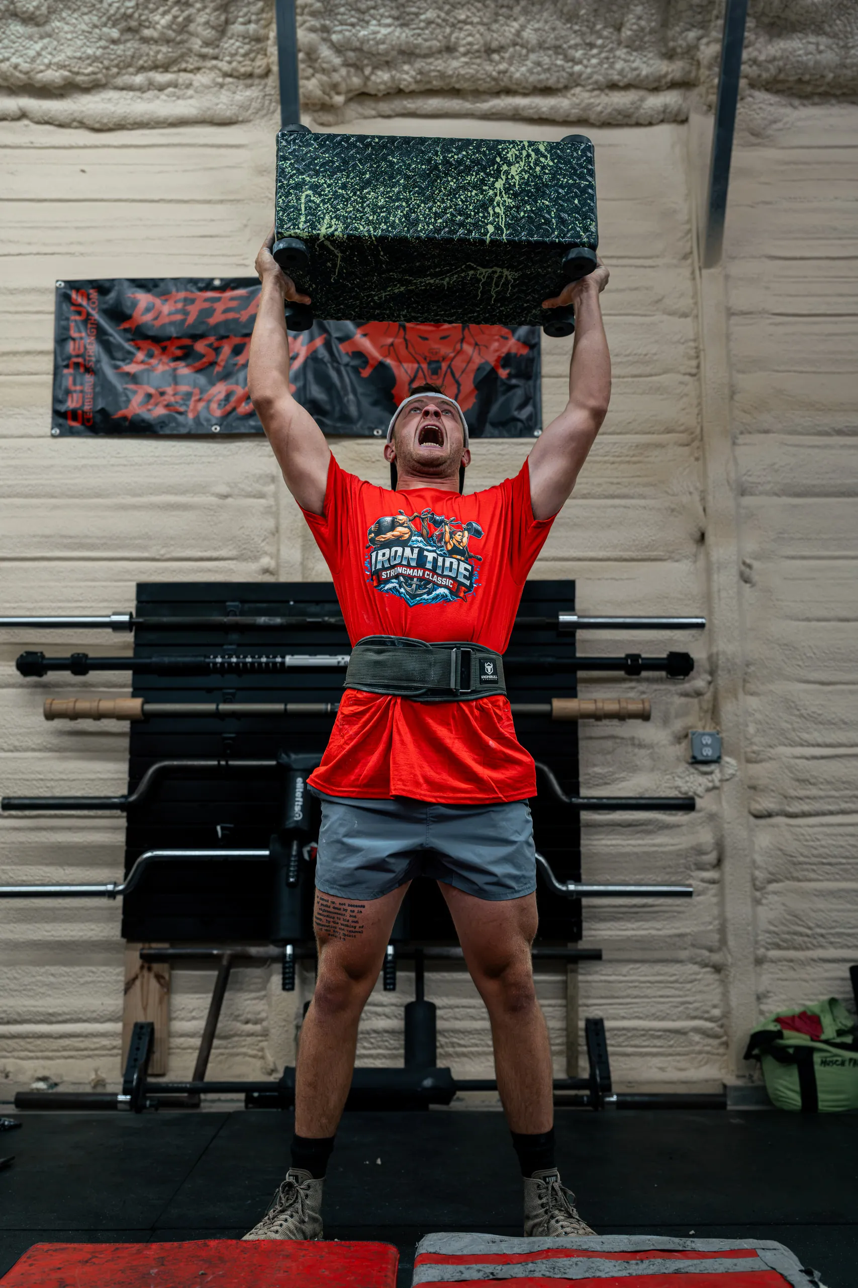 A competitor locks a sandbag block out overhead at the top of a press