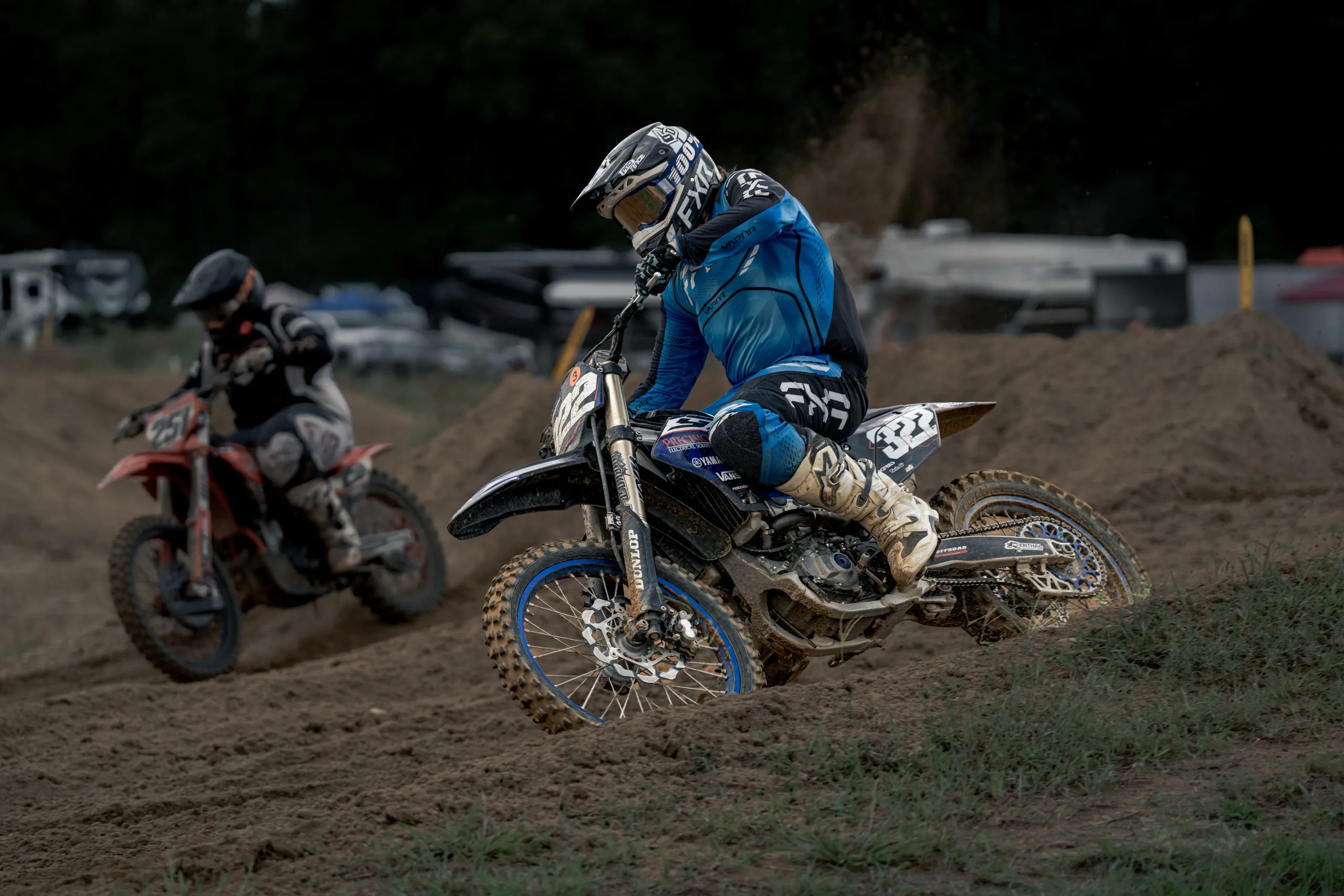 Two riders crest a rise together, the leader lifting the front wheel as the second bike tracks him through the dust