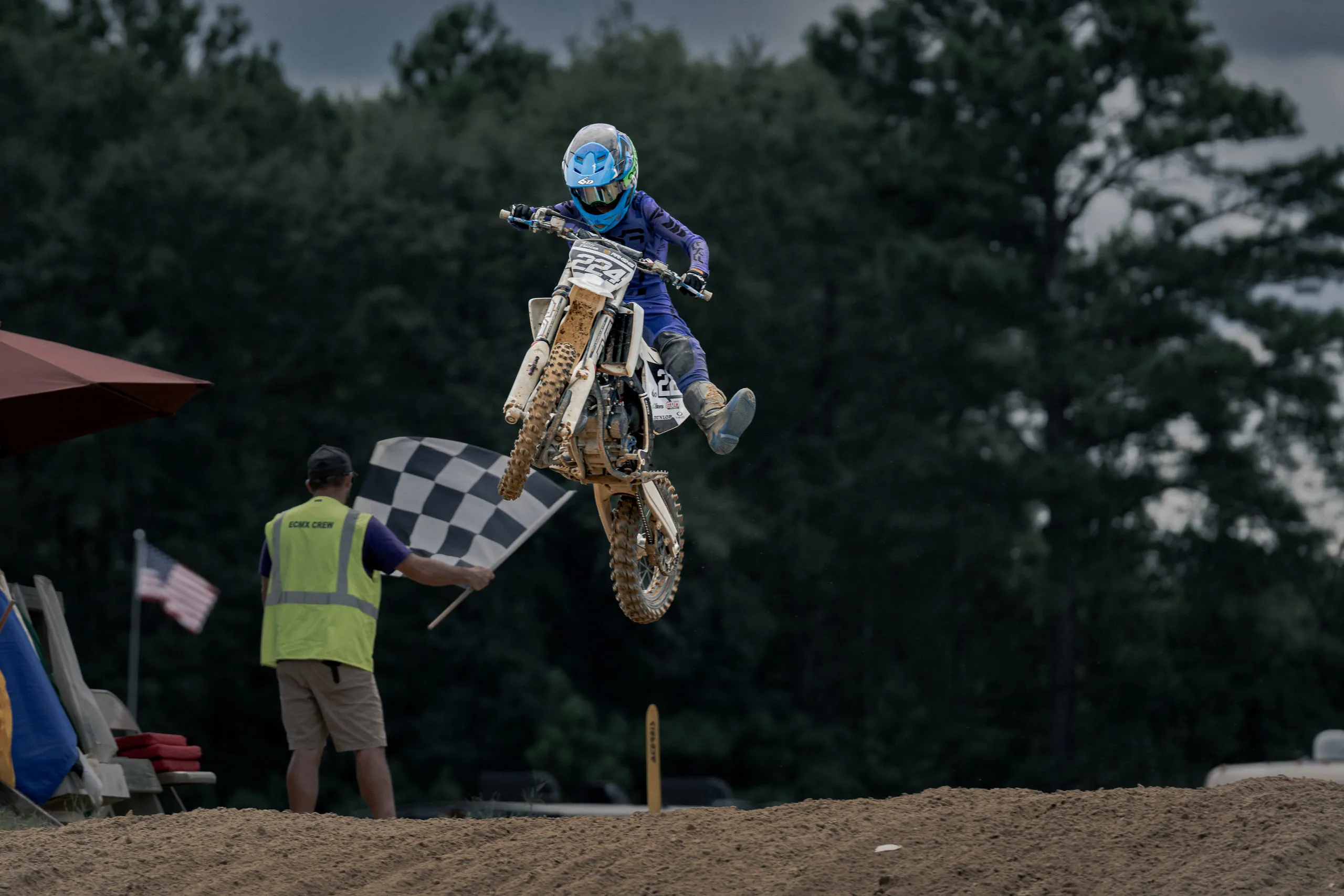 A young rider on a white Husqvarna flies past the official holding out the checkered flag