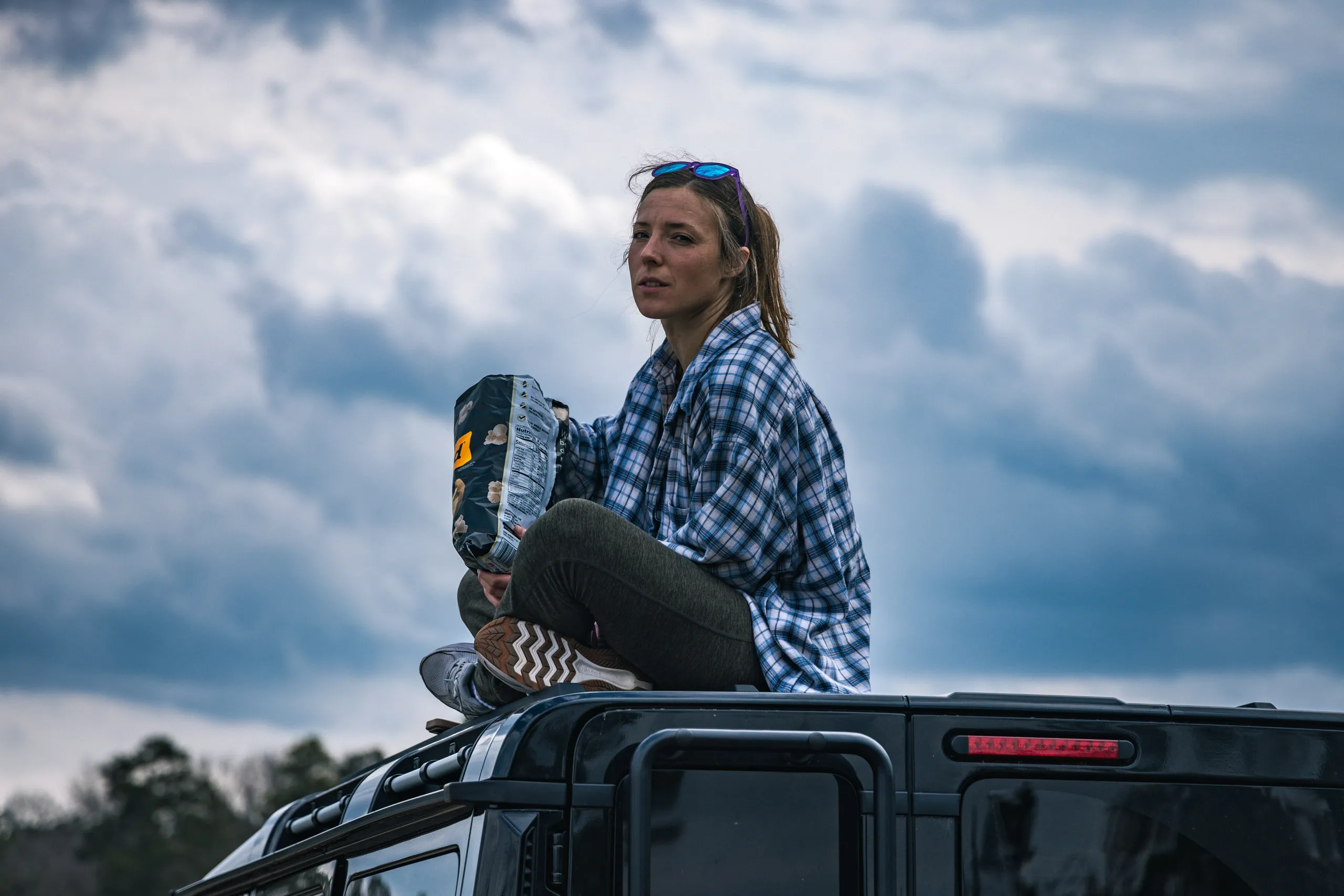 A woman sits on the roof of a pickup against a bank of storm clouds