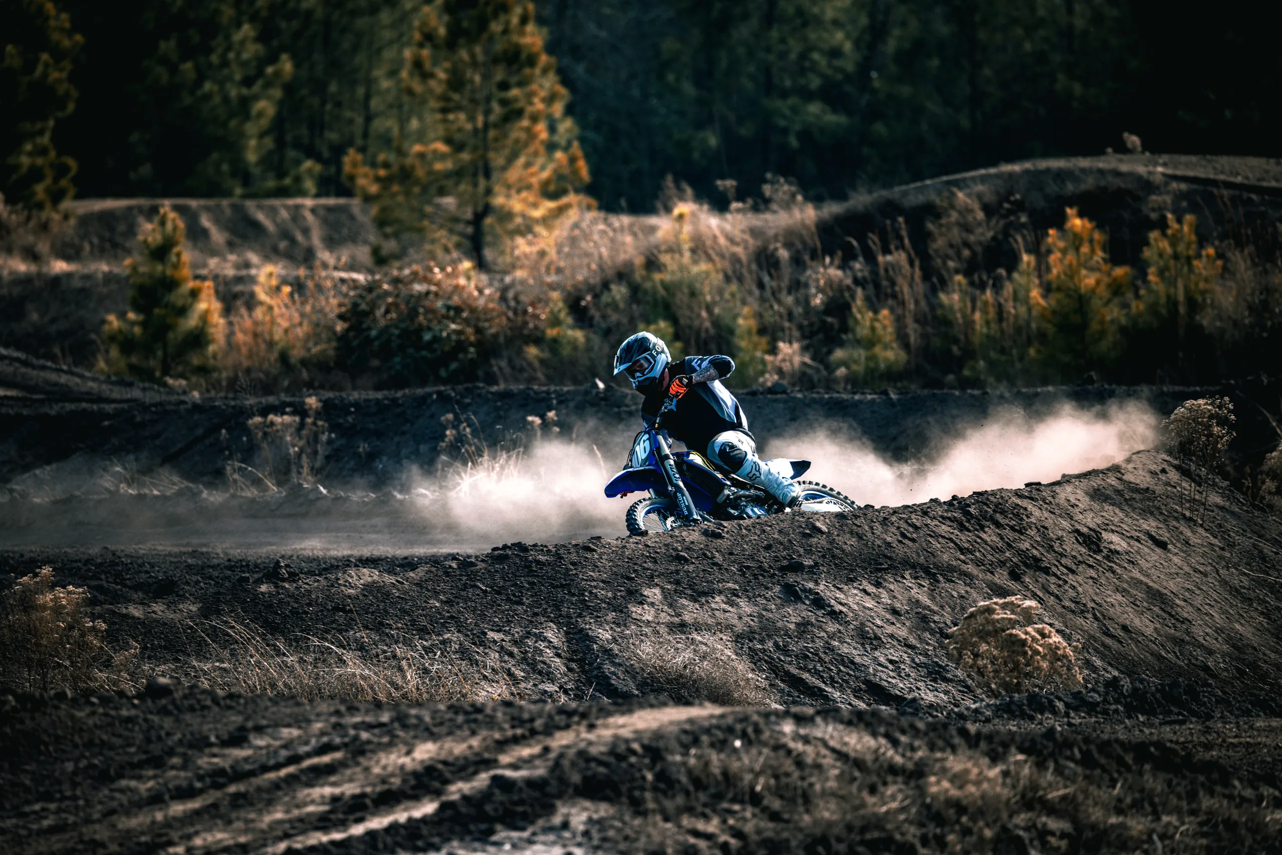A rider carves across a dark berm trailing a huge plume of white dust