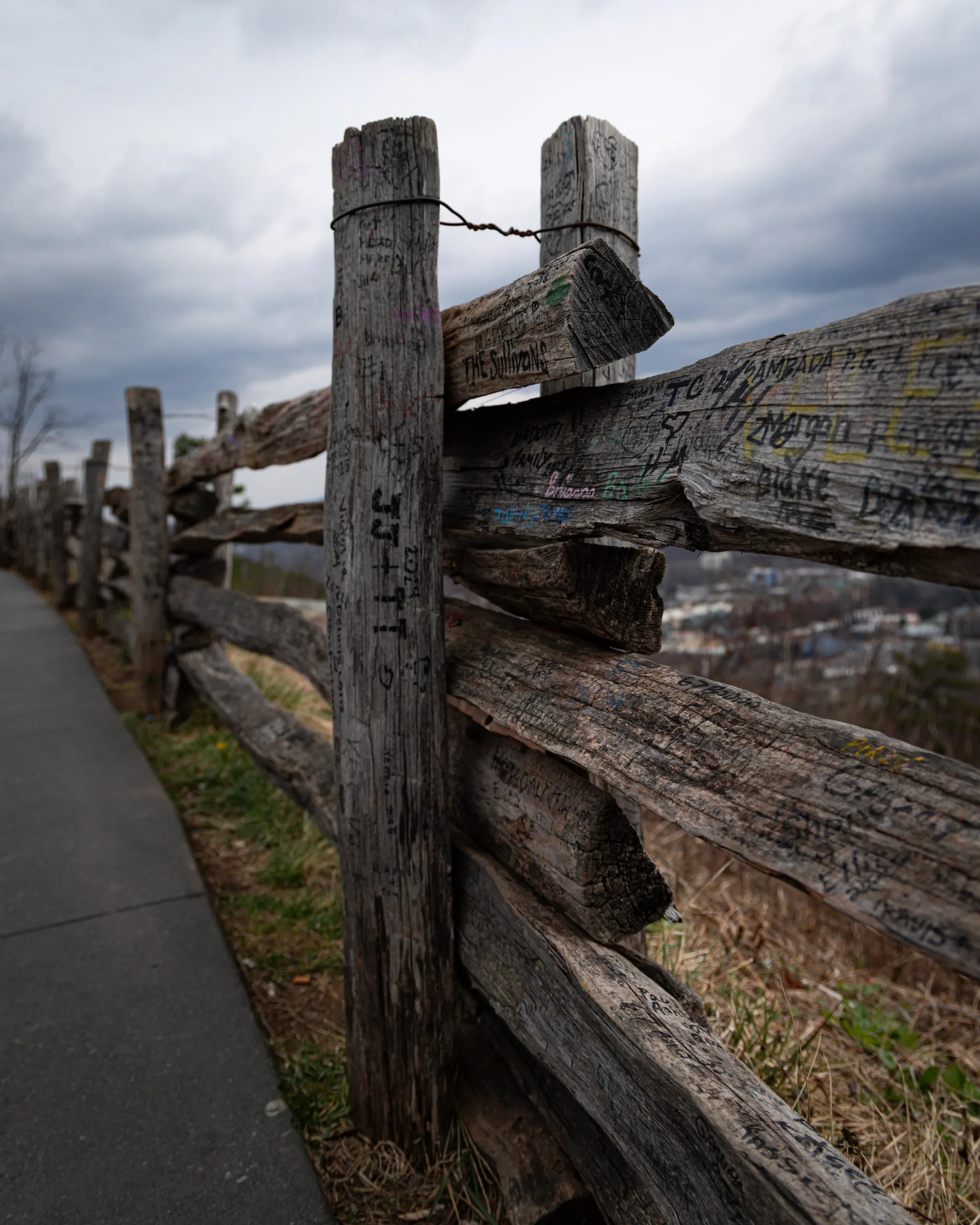 A weathered split-rail fence runs along a path under heavy cloud